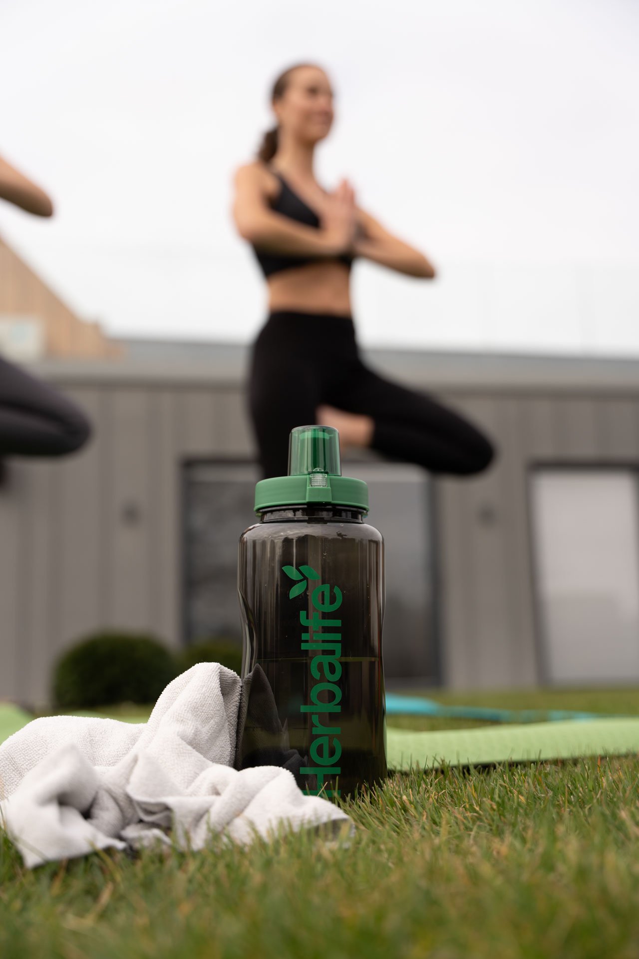 Botella de Herbalife con mujeres realizando yoga de fondo